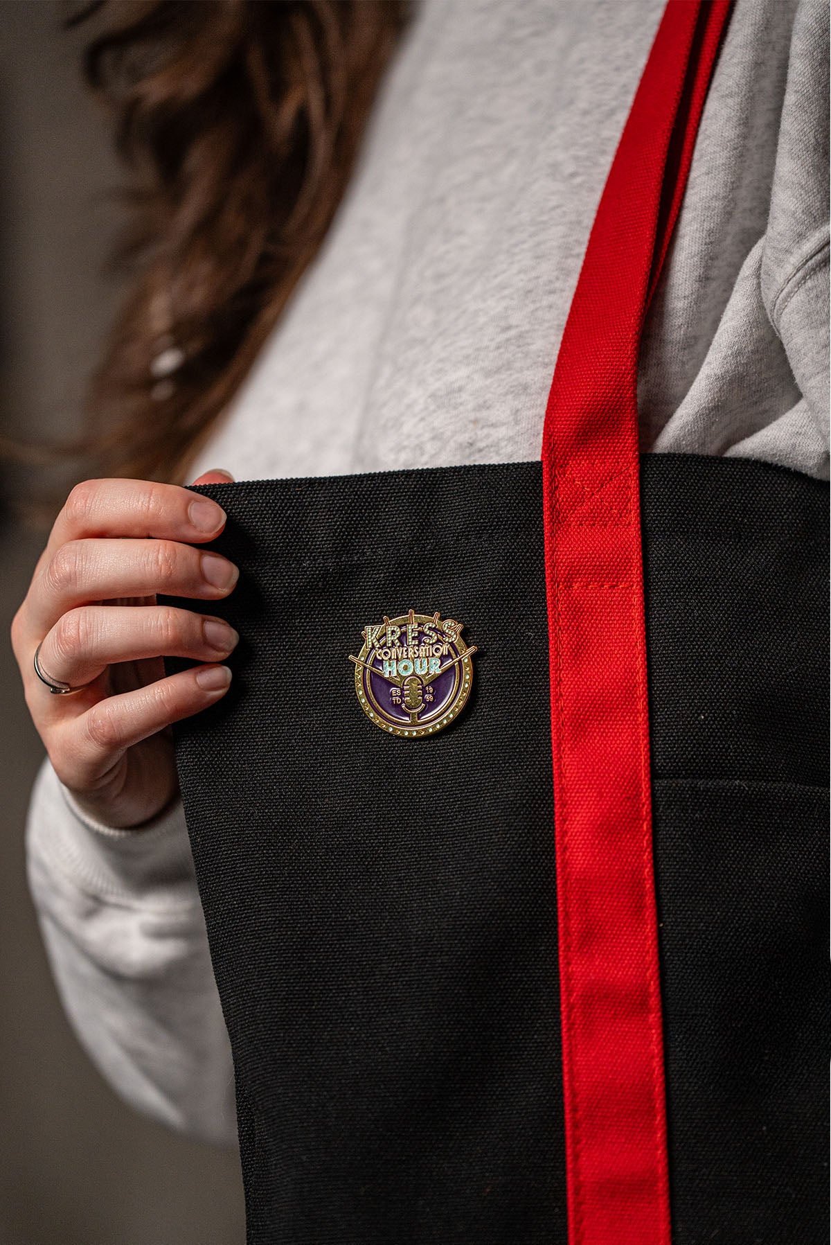 Person holding a black bag with a red strap and an enamle pin from Red Barrels