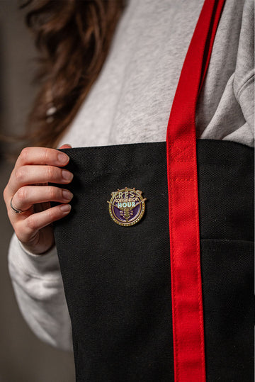 Person holding a black bag with a red strap and an enamle pin from Red Barrels